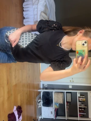 Svart blus med puffärm och broderi - Snygg svart blus med puffiga kortärmar och broderade håldetaljer på ärmarna. Rak passform och rund halsringning. Perfekt att styla med jeans eller kjol för en trendig look.