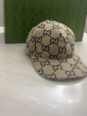 Beige GG keps i mocha material - Säljer en beige keps från GG med det klassiska GG-monogrammet i mörkbrunt över hela kepsen. Kepsen har böjd skärm och är tillverkad i ett tygmaterial som ger en exklusiv känsla. Perfekt accessoar för dig som vill sticka ut med en lyxig touch.