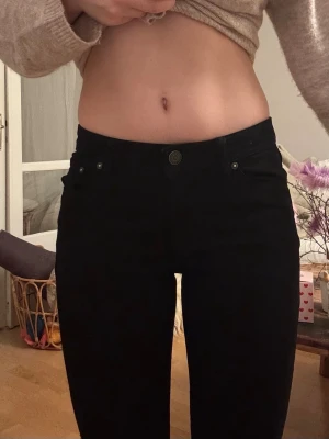 Svarta skinny jeans med hög midja - Säljer ett par svarta skinny jeans med hög midja och klassisk femficksmodell. Jeansen har en tajt passform och stängs med knapp och dragkedja. Perfekta till en enkel crop top eller stickad tröja. Jeansen har justerbara knappar på insidan av midjan för anpassad passform och personlig justering av midjestorleken.