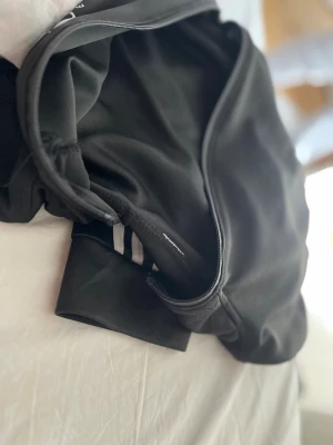 Svart hoodie med dragkedja - En svart hoodie med dragkedja framtill och ribbade muddar. Tillverkad i mjukt och stretchigt material som känns skönt mot huden. Klassisk design med huva och diskreta detaljer. Perfekt för en avslappnad och stilren look.