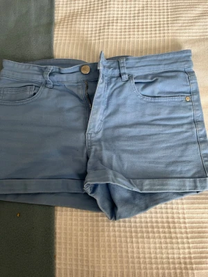 Ljusblå shorts från H&M - Snygga ljusblå shorts från H&M med klassisk femficksmodell, knapp och dragkedja framtill. Perfekta för varma dagar och har en enkel, stilren look som passar till det mesta. Gjorda i mjuk bomull för skön känsla.