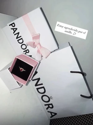 Pandora ring med röd hjärtformad sten - Säljer en elegant ring från Pandora med en hjärtformad röd sten i mitten, omgiven av små klara stenar. Ringen har en tunn, glittrande banddesign i silverfärg. Perfekt för dig som vill ha något romantiskt och stilrent.