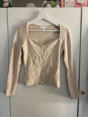 Beige ribbad topp från H&M - Säljer en beige ribbad topp från H&M med lång ärm och snygg v-ringad halsringning. Toppen har en figurnära passform och är tillverkad i mjukt material som passar perfekt till olika outfits.