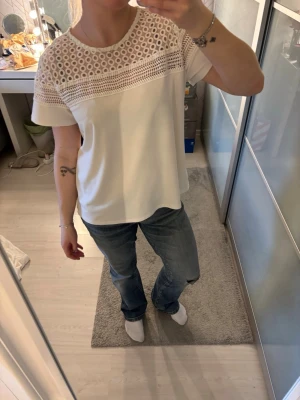 Vit blus med spetsdetaljer - Säljer en vit blus med rund hals och korta ärmar. Överdelen har snygga spets- och broderade detaljer som ger en fräsch och trendig look. Passformen är normal och materialet känns lätt och luftigt, perfekt för vår och sommar. Storlek s men kan passa någon men m också🥰