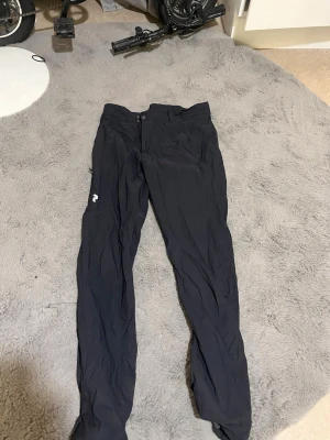 Svarta täckbyxor från Peak Performance - Säljer ett par svarta täckbyxor från Peak Performance. Byxorna har rak passform, dragkedja och knapp i midjan samt en liten logga på benet. Perfekta för kalla dagar och utomhusaktiviteter. Materialet är slitstarkt och vindtätt.
