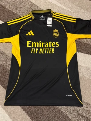 Real Madrid - Special Edition  - Säljs av ICEKIT  Storlek: M Namn + nummer: Inget Badge: Ingen  Här kan du se tröjor i ICEKIT Outlet. Alla tröjor är helt nya och utan några problem. Du kan välja att köpa dem här eller direkt via vår hemsida.  Tröjorna finns tillgängliga hos ICEKIT på: https://www.icekit.se  Länk: https://www.icekit.se/collections/outlet