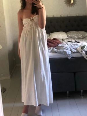 Vit maxiklänning med knytning - Säljer nu min vita maxiklänning med bandeau-topp och knytning framtill. Klänningen är i ett lätt, luftigt tyg och passar perfekt nu till sommaren💕Storlek S och är från HM. Säljs inte längre😇
