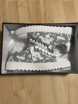 Gråvita sneakers från Numeris - Snygga sneakers från Numeris i grått och vitt med ett unikt kamouflagemönster. Skorna har vita, breda snören och en chunky, räfflad sula i vitt. Dom är helt nya och helt oanvända. Råkade få hem en storlek för lite 