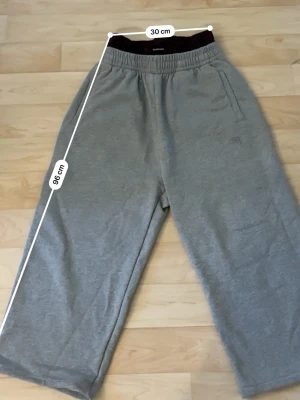 Gråa mjukisbyxor med resårmidja - Säljer ett par gråa mjukisbyxor med bred resår i midjan och sidofickor. Byxorna har en avslappnad passform och är tillverkade i mjukt sweatshirtmaterial. Perfekta för chill dagar hemma eller när du vill vara bekväm.