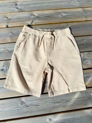 Beige linne shorts från Kappahl  - Snygga beige shorts med avslappnad passform och snörning i midjan. Tillverkade i ett mjukt bomullstyg som känns skönt mot huden. Shortsen har två sidofickor och en enkel, stilren design som passar perfekt till sommaren.