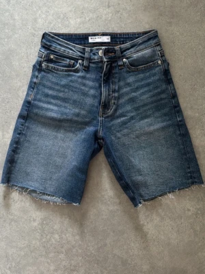 Blå mom fit jeansshorts XS - Säljer ett par blå mom fit jeansshorts i klassisk femficksmodell. Shortsen har hög midja, råa kanter nertill och dragkedja med knapp. Perfekta för sommaren och ger en avslappnad vibe till din outfit.