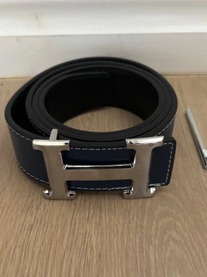 H bälte  - Säljer nu ett riktigt snyggt bälte med den ikoniska H loggan på framsidan! | Väldigt bra skick, nyskick? | Passar bra till fest-vardag. | Mörkblå färg, möjligt att använda det utan och in där det blir svart. | Storlek 115. | Släng iväg en signal vid funderingar så svarar jag snabbt. |