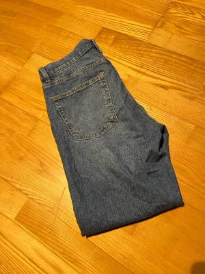 Blå raka jeans med klassisk passform - Säljer ett par blå jeans med rak passform och klassisk femficksdesign. Jeansen har en normal midja och är tillverkade i denim. Perfekta för dig som gillar en enkel och tidlös stil. Storlek W32, L30. Säljer för 200kr.