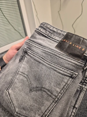 Grå Levi's Line 8 jeans med rå kant W29 L30 - Säljer ett par grå Levi's Line 8 jeans i tvättad look. Jeansen har raka ben med rå, fransad kant nertill och klassiska fem fickor. Materialet är denim i bomull och passformen är slim. Perfekta för en avslappnad och trendig stil.