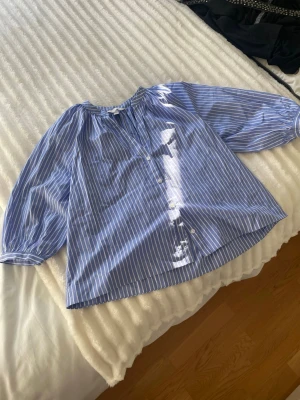 Blåvit randig blus med knappar - Blus i blått med vita vertikala ränder och knäppning framtill. Modellen är lös och har rund halsringning samt trekvartsarmar.🤗