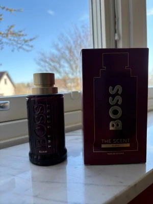 BOSS The Scent Elixir parfym - BOSS The Scent Elixir är en intensiv parfym med en mörkröd glasflaska och guldfärgad kork. Flaskan har en elegant och robust design med BOSS-loggan i guld på framsidan. Parfymen levereras i en matchande mörkröd kartong med guldtryck. Nypris 1700 kr
