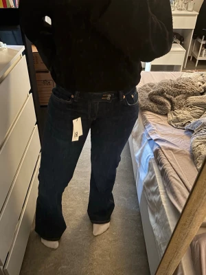 Mörkblå bootcut jeans  - Säljer ett par mörkblå bootcut jeans med klassisk femficksdesign och snygga kontrastsömmar. Jeansen har hög midja och är tillverkade i ett mjukt denimtyg som sitter skönt. Perfekta för dig som gillar en tidlös och avslappnad look. Storlek M short 