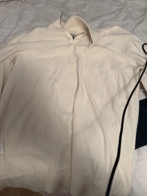 Beige tröja med krage - En stilren beige tröja med krage och lång ärm. Tröjan har ribbade muddar vid ärmslut och nederkant, vilket ger en snygg och bekväm passform. Perfekt för dig som gillar en enkel och klassisk look. Från volt, sitter som en M
