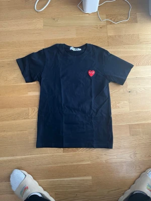 Marinblå Comme des Garçons PLAY t-shirt - Marinblå t-shirt från Comme des Garçons PLAY med det ikoniska röda hjärtat broderat på bröstet. Klassisk passform med rund hals och korta ärmar. Tillverkad i mjuk bomull som känns skön mot huden. Har använts  2-3 gånger är som ny