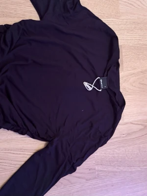 Svart långärmad topp från Gina tricot  - En stilren svart långärmad topp från Gina. Toppen har en enkel och tight passform med lätt rynkade detaljer på sidorna. Tillverkad i mjukt och stretchigt material som känns skönt mot huden. Perfekt att matcha med jeans eller kjol.