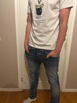 Blå slitna slim fit jeans - Säljer ett par blå slim fit jeans med slitningar och hål på benen. Jeansen har klassisk femficksdesign och en snygg tvättad look. Perfekta för dig som gillar en avslappnad och trendig stil. Storlek 32-32!