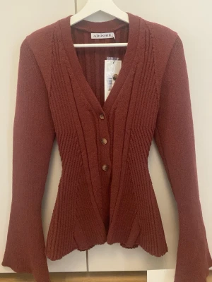 Burgundy ribbad kofta från Adoore - Figurnära kofta från Adoore med lappar kvar. Ger en fin timglas form. Aldrig använd. Kommer från ett djur och rökfritt hem! Kan prutas vid snabb affär! 