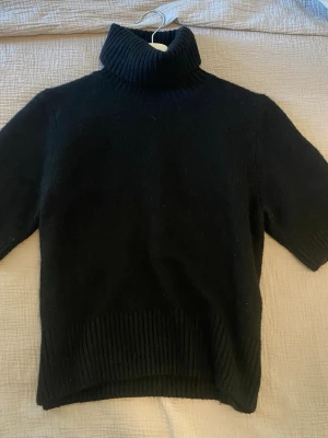 Svart polotröja från H&M - Svart stickad tröja med polokrage och kortare ärm. Från H&M, använd ca två gånger och kommer från ett djur och rökfritt hem! Passar både S och M personer.