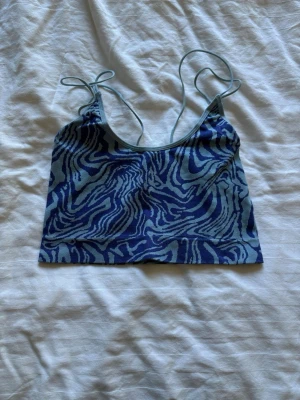 Blå zebramönstrad topp - Snygg blå linnetopp med zebramönster och tunna axelband. Toppen har en croppad passform och är perfekt för varma dagar. Materialet känns mjukt och stretchigt, vilket gör den bekväm att bära. Perfekt att styla med jeans eller kjol.