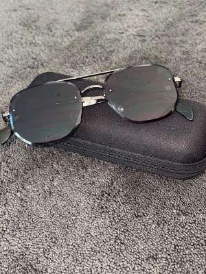 Svarta fyrkantiga solglasögon - Snygga svarta solglasögon för barn med fyrkantiga glas och metallbågar. Kommer med ett svart hårt fodral som skyddar glasögonen när du inte använder dem. Perfekta för soliga dagar och ger en cool look.