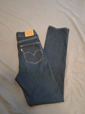 Levi's 724 High Rise Straight jeans - Mörkblå Levi's 724 High Rise Straight jeans med klassisk femficksdesign och raka ben. Jeansen har hög midja, tydliga kontrastsömmar och Levi's ikoniska läderpatch bak. Tillverkade i denim med en snygg tvätt och diskret logga på bakfickan.