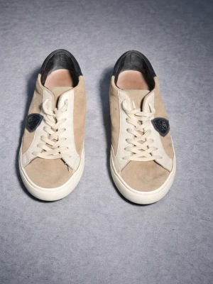phillipe model skor  - Snygga beige sneakers i mocka med vita detaljer från Phillipe model. Skorna har en svart logotyp på sidan och svarta detaljer vid hälen. Klassisk låg modell med vita snören och gummisula. Perfekta för en stilren och avslappnad look.
