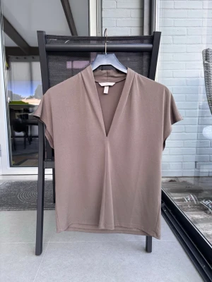 Brun v-ringad topp med kort ärm/ festtopp sommartopp - En stilren brun topp med v-ringning och korta ärmar. Toppens enkla design gör den lätt att matcha och den har en lös passform. Perfekt för dig som gillar minimalistisk stil.