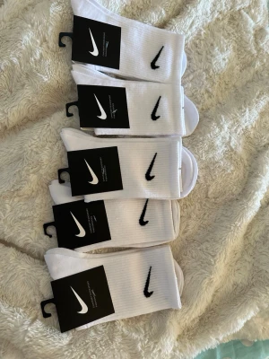 Vita  strumpor med svart logo - Klassiska vita strumpor med den ikoniska svarta swoosh-loggan broderad på sidan. Strumporna är ribbade och tillverkade i mjuk bomullsmix som sitter skönt på foten. Perfekta till sneakers och streetwear.