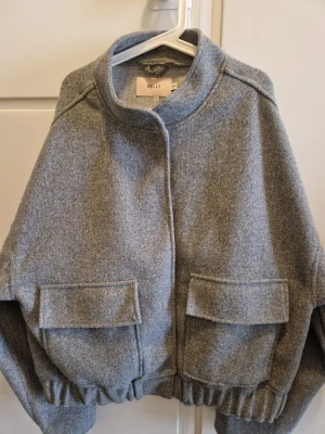 Grå jacka från Nelly - Snygg grå jacka från Nelly med oversized passform, stora fickor framtill och elastisk nederkant. Jackan har en hög krage och stängs med knappar. Perfekt för lager-på-lager och en chill streetstyle-look.