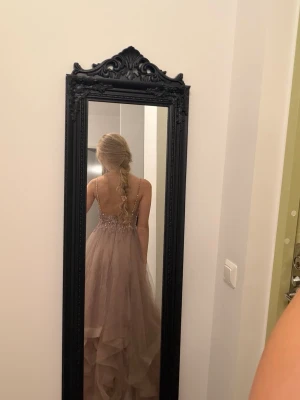 Ljusrosa långklänning med spetsdetaljer - Romantisk ljusrosa långklänning med tunna axelband, v-ringad spetsliv och volangig kjol i flera lager tyll. Perfekt för bal eller speciella tillfällen. Kjolen har vacker fall och toppen är dekorerad med broderade detaljer. Storlek 34