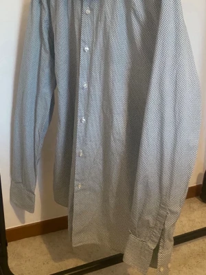 Boss Blå prickig skjorta med knappar - Säljer en boss blå skjorta med små vita prickar och klassisk knappstängning. Skjortan har långärmad design och breda manschetter med knappar. Perfekt för dig som gillar stilrena mönster och enkel look.