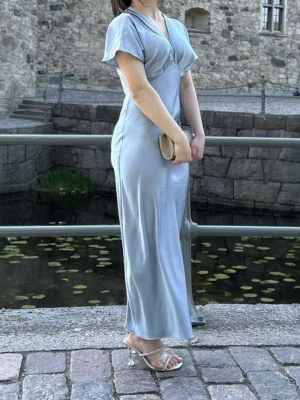 Ljusblå ZARA långklänning i satin  - Elegant ljusblå långklänning i glansigt satinliknande material. Klänningen har korta ärmar, v-ringad hals och en mjukt åtsittande passform som ger en snygg siluett. Perfekt för student eller sommarens festligheter.