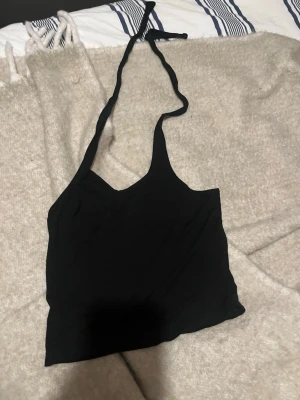 Svart halterneck linnetopp - Snygg svart linnetopp med halterneck och croppad passform. Perfekt till jeans eller kjol för en trendig look. Tunn och lätt, passar bra till varma dagar.