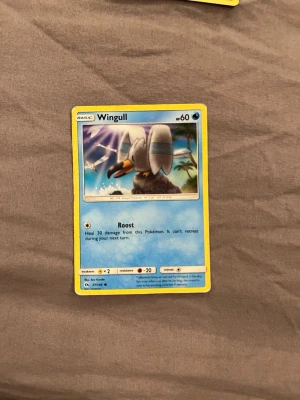 Wingull Pokémonkort - Säljer ett Wingull Pokémonkort med blå bakgrund och gul ram. Kortet har en illustration av Wingull, en fågelliknande Pokémon, och innehåller information om attacken Roost. Perfekt för samlare eller Pokémon-fans.