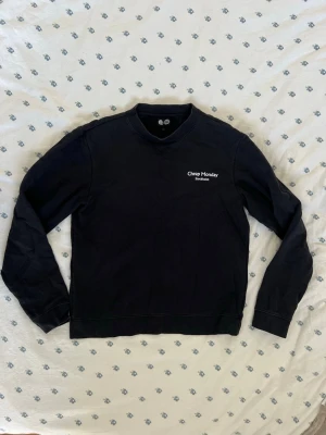 Svart sweatshirt från Cheap Monday - En svart sweatshirt från Cheap Monday med vit logga och texten 'Stockholm' på bröstet. Tröjan har rund halsringning och långa ärmar. Tillverkad i mjukt bomullsmaterial och har en enkel, stilren design som passar till det mesta. Storlek S / Small. Måtten finns. 