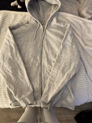 Ljusgrå zip hoodie med huva - En basic ljusgrå hoodie med dragkedja från Weekday. Hoodien har en klassisk passform, två fickor framtill, ribbade muddar och snören i huvan. Tillverkad i mjuk bomullsblandning som är skön att ha på sig.