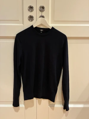 Svart stickad tröja från Uniqlo - En stilren Mörk blå stickad tröja från Uniqlo med rund halsringning och långa ärmar. Tröjan har en enkel och klassisk design som passar till det mesta. Materialet består av merinoull och är mjukt och tunt, perfekt för lager på lager. Tröjan har använts sparsamt.