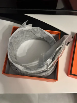 Grått bälte med silverdetaljer - Stilrent grått bälte med silverfärgat spänne, levereras i en orange ask. Perfekt accessoar för att lyfta din outfit med en clean och modern look.  110 cm 
