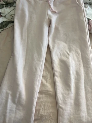 Ljusrosa mjukisbyxor med dragsko - Säljer ett par ljusrosa mjukisbyxor med dragsko i midjan och raka ben. Byxorna har en enkel och clean look, perfekta för chill dagar hemma eller när du vill vara bekväm. Tillverkade i mjukt och skönt material som känns nice mot huden.