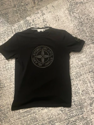  Stone Island t shirt - Snygg svart t-shirt från Stone Island med det ikoniska kompassloggan broderad på bröstet. Klassisk passform och rund halsringning. Tillverkad i mjuk bomull som känns skön mot huden. Perfekt för dig som gillar streetwear och vill ha en stilren look.