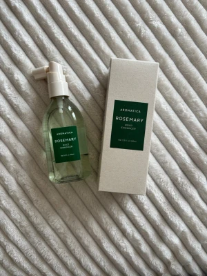 Aromatica Rosemary Root Enhancer - Aromatica Rosemary Root Enhancer är en hårprodukt i en genomskinlig plastflaska med vitt spraymunstycke och grön etikett. Produkten innehåller 100 ml och levereras med en beige kartong. Perfekt för dig som vill boosta hårbotten med rosmarinextrakt.