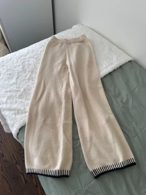 Beige stickat set med svart kant - Mysig beige stickat set med bred resår i midjan och raka ben. Nederkanten har en snygg svart och vit randig detalj som ger extra stil. Perfekta för chill dagar hemma eller när du vill vara bekväm men ändå se trendig ut.