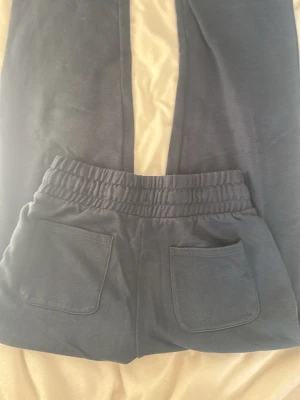 Mörkblå mjukisbyxor med fickor - Säljer ett par mörkblå mjukisbyxor med resår i midjan och två stora bakfickor. Byxorna har en avslappnad passform och är gjorda i mjukt bomullsmaterial, perfekta för chill dagar. Enkla att matcha med hoodie eller t-shirt. Har ett litet hål vid den högra fickan