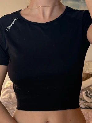 Svart croppad topp ICANIWILL - Snygg svart crop top från ICANIWILL med korta ärmar och tight passform. Tillverkad i ett stretchigt funktionsmaterial som passar perfekt till träning. Diskret logga på axeln och ryggen 🖤