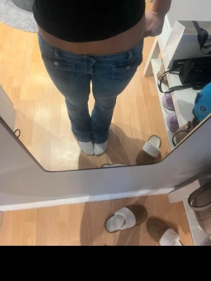 Blå low waist bootcut jeans - Säljer ett par blå bootcut jeans med låg midja och snygga fickdetaljer med lock och knapp bak. Jeansen har klassisk femficksdesign och är gjorda i denim med lätt tvättad look. Perfekta för dig som gillar en avslappnad och trendig stil.